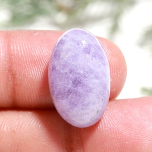 May include: An oval-shaped, polished gemstone with a translucent, light lavender-purple color and a textured, crystalline interior structure. The stone features a smooth, rounded surface with visible internal inclusions and a soft, glossy finish.