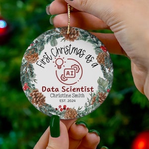 May include: A round Christmas ornament with a green, white, and brown wreath design. The ornament features the text "First Christmas as a Data Scientist" with a light bulb and gears icon. The text "Christine Smith EST. 2024" is also included.