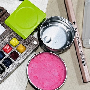 May include: A set of watercolour paints in a wooden palette with a green clip, a silver container with a pink substance, and a wooden pencil with the text "Return to nature 木之森 2B".