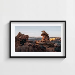 Può includere: Fotografia incorniciata di un paesaggio desertico con formazioni rocciose di arenaria. L'immagine cattura la bellezza naturale del terreno, con toni caldi e un cielo limpido. La cornice nera aggiunge un tocco moderno all'opera.