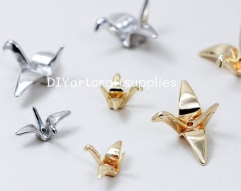 May include: A collection of small, metallic origami crane figurines in silver and gold. The cranes are arranged on a white surface, with the text "DIYartcraftsupplies" visible. The cranes vary in size and are in various stages of flight.