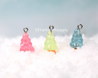 Pode incluir: Três pequenos pingentes de árvore de Natal transparentes em rosa, amarelo e azul. Cada pingente tem um laço prateado para pendurar.