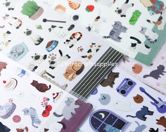 May include: A collection of cat-themed stickers in various poses and colors, including calico, gray, and black and white cats. The stickers feature additional elements like food bowls, beds, and musical instruments. The text "DIYartcraftsupplies" is visible.
