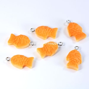 May include: Six orange fish-shaped charms with silver jump rings. The charms are made of polymer clay and have a textured surface.