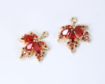 May include: Two gold-tone maple leaf charms with red crystal accents. Each charm has a loop for attaching to jewelry.