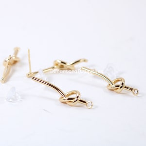 May include: Gold knot earring findings with a loop at the end. The findings are on a white surface.