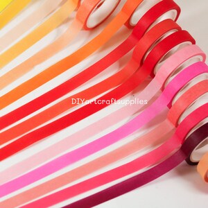 May include: A collection of 15 rolls of washi tape in various shades of orange, red, pink, and purple. The tape is arranged in a rainbow pattern, with the lightest colors at the top and the darkest colors at the bottom. The tape is all the same width and has a matte finish.