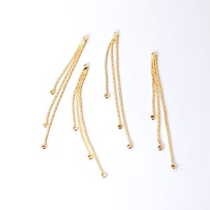 Puede incluir: Tres colgantes de borla de cadena dorada con un bucle en la parte superior y pequeñas cuentas redondas en la parte inferior.