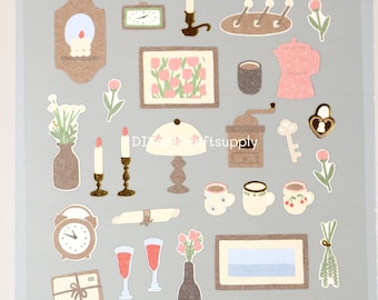 May include: A sheet of vintage-style stickers featuring illustrations of home decor, flowers, and other objects. The stickers are printed on a beige background with a textured paper look. The stickers include a clock, a lamp, a coffee pot, a key, a vase of flowers, a candle, a rolling pin, a bottle of wine, a picture frame, and more.