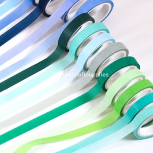 May include: A collection of 12 washi tapes in shades of blue and green. The tapes are arranged in a gradient from dark blue to light green.  The tapes are all 15mm wide and are made of high-quality washi paper.