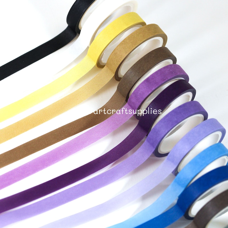 May include: A set of ten washi tapes in various colors, including black, yellow, brown, purple, blue, and brown. The tapes are arranged in a fan shape, with the black tape at the top and the brown tape at the bottom.