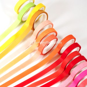 May include: A set of 10 washi tapes in a rainbow gradient of colors, starting with yellow and ending with pink. The tapes are arranged in a fan shape, with the yellow tape at the top and the pink tape at the bottom. The tapes are all 15mm wide and are made of high-quality paper.