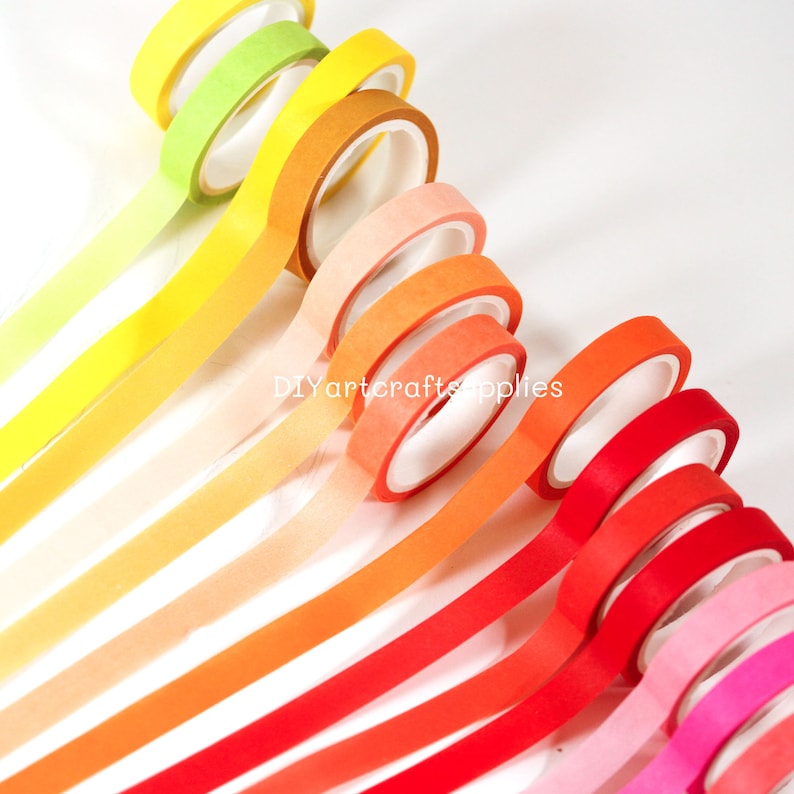 May include: A set of 10 washi tapes in a rainbow gradient of colors, starting with yellow and ending with pink. The tapes are arranged in a fan shape, with the yellow tape at the top and the pink tape at the bottom. The tapes are all 15mm wide and are made of high-quality paper.