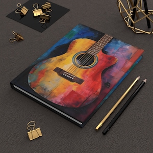 May include: A colourful, abstract painting of an acoustic guitar on a black notebook cover. The guitar is painted in shades of red, yellow, blue, and green.