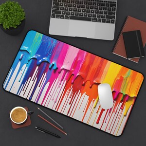 May include: A colorful mouse pad with a design of dripping paint in shades of blue, pink, yellow, orange, and red. The mouse pad is on a black surface with a computer keyboard and a notebook.