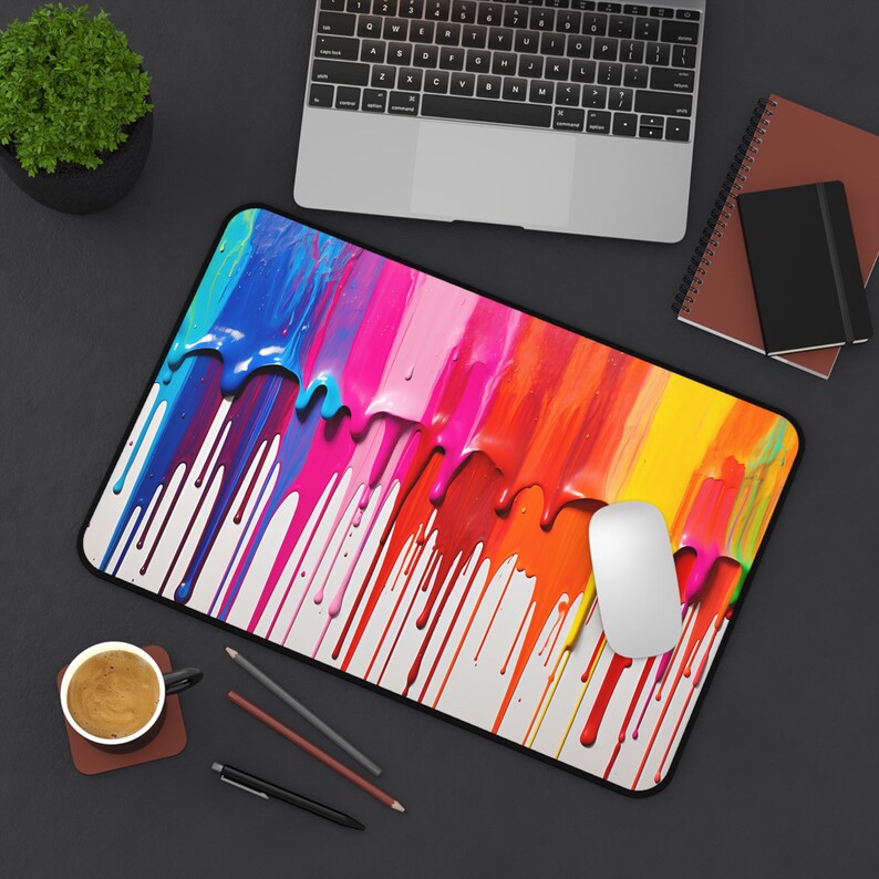 May include: A colorful mouse pad with a design of dripping paint in shades of blue, pink, yellow, orange, and red. The mouse pad is on a black surface with a laptop and a notebook.