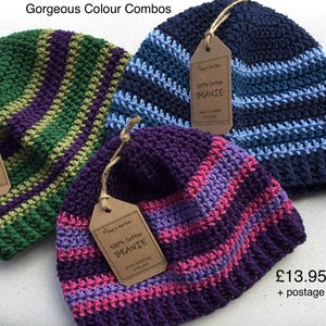 May include: Three hand-crocheted beanies made of 100% cotton. One beanie features green and purple stripes, another has dark blue and light blue stripes, and the third displays purple, magenta, and light pink stripes. Each has a brown paper tag.