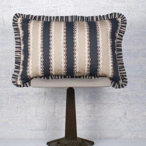 May include: A decorative cushion with a black and beige striped pattern and a brown wavy line design. The cushion has a ruffled edge and is sitting on a vintage Singer sewing machine stand.