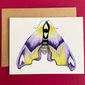 May include: A greeting card featuring a hand-drawn moth illustration. The moth has purple, yellow, and white wings with a black and white body. The card is paired with a brown envelope, set against a magenta background.