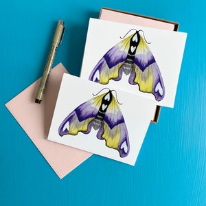 May include: Two blank greeting cards with a purple and yellow butterfly illustration on each. The butterflies have white heart-shaped markings on their wings.