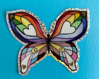 May include: A rainbow-coloured butterfly sticker with a glittery border and gold hearts. The butterfly's wings are made up of different colours of the rainbow, and the hearts are scattered throughout the wings.