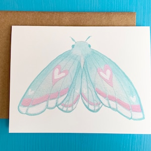 May include: A light blue butterfly with pink accents and white hearts on its wings. The butterfly is painted on a white card.