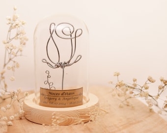May include: A silver wire rose sculpture inside a clear glass dome on a wooden base. The base has a label that reads "Noces d'etain Gregory & Angelique 11 ans 16.07.2014 - 16.07.2025".