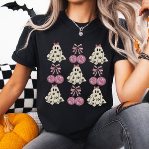 Puede incluir: Camiseta negra con un estampado gr&aacute;fico de fantasmas y bolas de discoteca rosas con lazos. Los fantasmas llevan patrones florales.