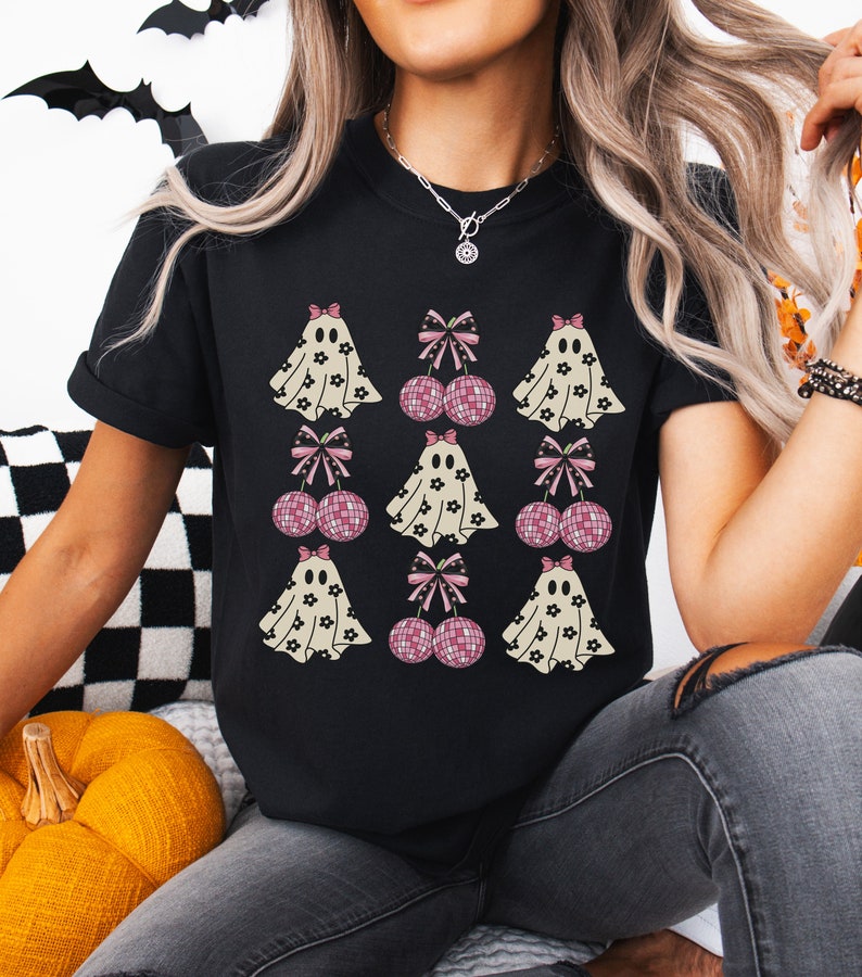 Puede incluir: Camiseta negra con un estampado gr&aacute;fico de fantasmas y bolas de discoteca rosas con lazos. Los fantasmas llevan patrones florales.