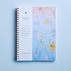 May include: A spiral-bound 2027 planner titled Reverie with a white vertical spine section listing features and a light blue to pink gradient cover featuring delicate line art of flowers with yellow and pink watercolor accents.