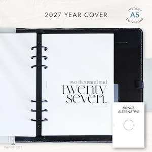 Puede incluir: Una carpeta negra de seis anillas que contiene papel blanco con el texto "two thousand and twenty seven". Un pequeño recuadro muestra un diseño de portada alternativo con texto circular. La parte superior incluye "2027 YEAR COVER" e "INSTANT A5 DOWNLOAD".