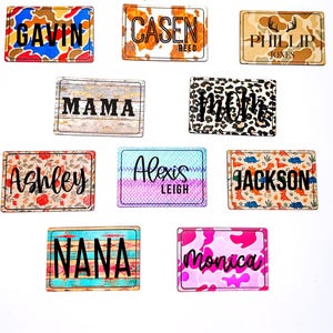 May include: A collection of rectangular name tags with various patterns and names. Designs include camouflage, cow print, floral, wood grain, and animal print. Names include "Gavin", "Cason Reed", "Phillip Jones", "Mama", "Mom", "Ashley", "Alexis Leigh", "Jackson", "Nana", and "Monica".