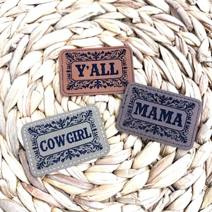 May include: Three rectangular patches with decorative borders and text. The top patch is brown and reads "Y'ALL". The bottom left patch is gray and reads "COWGIRL". The bottom right patch is gray and reads "MAMA".