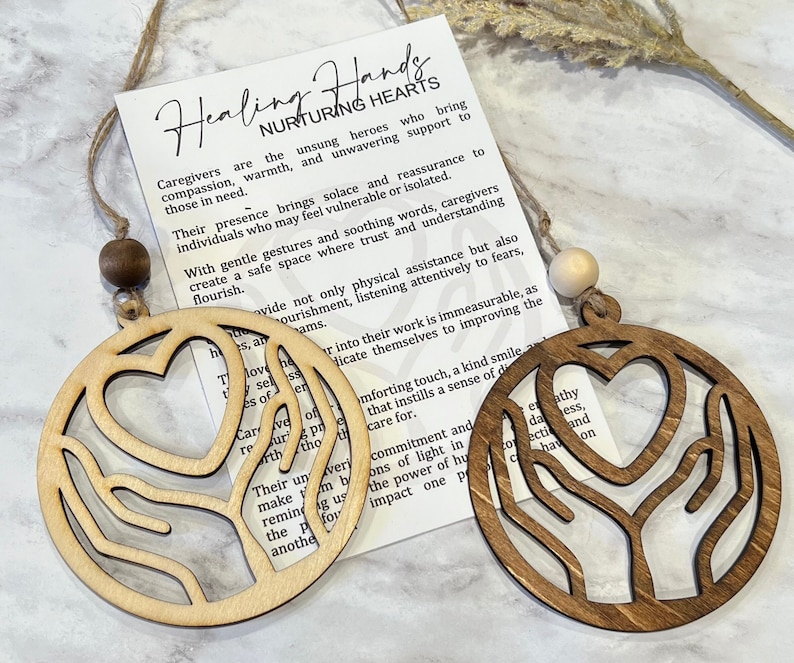 May include: Two wooden ornaments featuring a heart and hands design. The ornaments are brown and natural wood. The text on the card reads "Healing Hands Nurturing Hearts".
