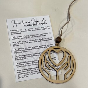 May include: Wooden ornament featuring a heart and two hands, representing healing and nurturing hearts. The ornament is beige and has a twine string for hanging. The text on the card reads "Healing Hands Nurturing Hearts". Caregivers are the unsung heroes who bring compassion, warmth, and unwavering support to those in need.