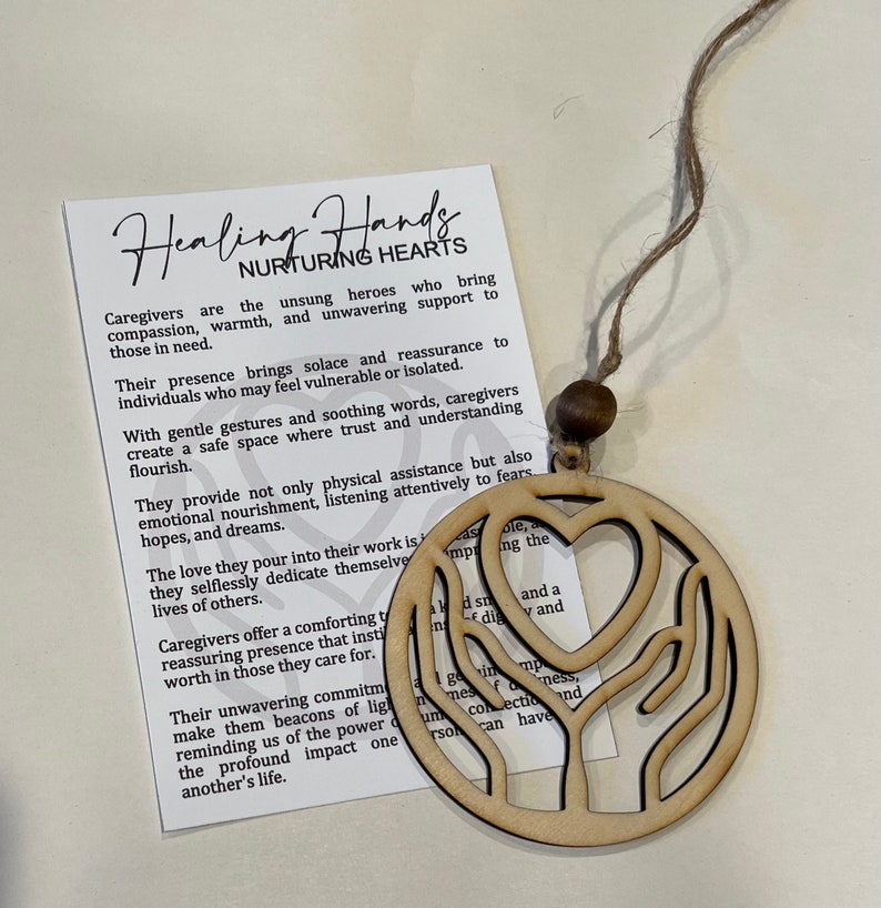 May include: Wooden ornament featuring a heart and two hands, representing healing and nurturing hearts. The ornament is beige and has a twine string for hanging. The text on the card reads "Healing Hands Nurturing Hearts". Caregivers are the unsung heroes who bring compassion, warmth, and unwavering support to those in need.