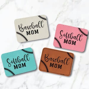 May include: Four leather keychains with stitched baseball seams. The keychains are in beige, pink, teal, and brown. Each keychain has a different text: "Baseball MOM", "Softball MOM", "Softball MOM", and "Baseball MOM".