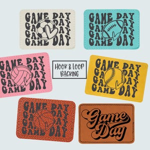 May include: A collection of rectangular patches with the words "Game Day" in a retro font. Each patch features a different sports ball: soccer, football, volleyball, baseball, and basketball. The patches come in various colors, including cream, teal, pink, yellow, and brown.