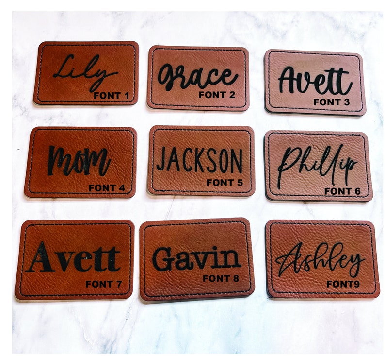 May include: Nine rectangular brown leather patches with black text. The patches display names such as "Lily", "Grace", "Avett", "Mom", "Jackson", "Phillip", "Gavin", and "Ashley". Each patch has a different font style and the text "FONT" followed by a number.