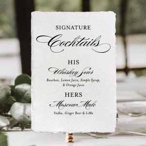 May include: A rectangular white paper menu with deckled edges featuring black printed text that reads SIGNATURE Cocktails, HIS Whiskey Sour with Bourbon, Lemon Juice, Simple Syrup, & Orange Juice, and HERS Moscow Mule with Vodka, Ginger Beer & LiMe.