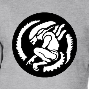 May include: A light grey t-shirt with a black and white graphic of an alien creature inside a black circle. The alien is crouching, encircled by a segmented tail design. The shirt is made of a soft material.