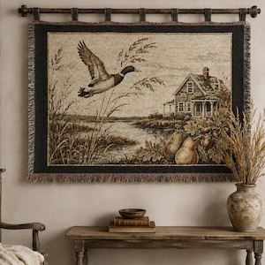 May include: A rectangular woven wall tapestry featuring a mallard duck in flight over a marshy landscape with tall grasses, a house in the background, and a foreground arrangement of two pears and acorns, finished with a dark border and fringe.