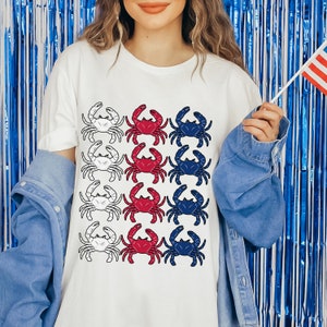 May include: White t-shirt with a design of red, white, and blue crabs arranged in a pattern resembling the American flag.
