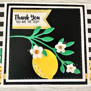 May include: A handmade greeting card with a black background and a yellow lemon illustration. The card features the text "Thank You, You Are The Zest!" in a banner. Green leaves and white flowers with yellow centers decorate the lemon.