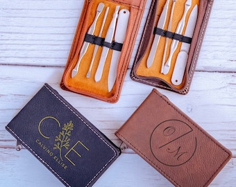 May include: Two open brown leather manicure kits with stainless steel tools, including scissors, nail clippers, and cuticle pushers. Two small leather cases with embossed initials and the text "CALVINO FELICE" are also visible. Pink flowers are scattered around.