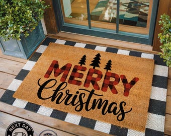 May include: A rectangular coir doormat with a black and white checkered border. The center features the words "MERRY Christmas" in black script and red plaid block letters, with three black tree silhouettes above the word "MERRY".