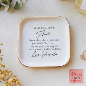 May include: White ceramic trinket tray with a gold rim. The tray has a message that reads "To my beautiful Aunt You've always been more than just family. You've been my safe place, my support and someone I'll always admire. Love, Jacquelin"