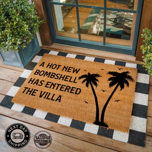 May include: A rectangular tan coir doormat featuring the black text A HOT NEW BOMBSHELL HAS ENTERED THE VILLA, accompanied by black silhouettes of two palm trees and several small birds, layered over a black and white checkered floor mat.