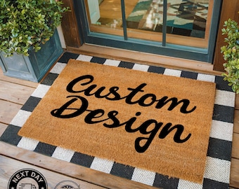 May include: A brown coir doormat with a black and white checkered border. The text "Custom Design" is printed in black cursive font on the doormat.