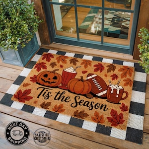 May include: A rectangular doormat with a black and white checkered border. The mat features a fall-themed design with pumpkins, a football, and mugs of hot chocolate. The text "Tis the Season" is printed in a decorative font.